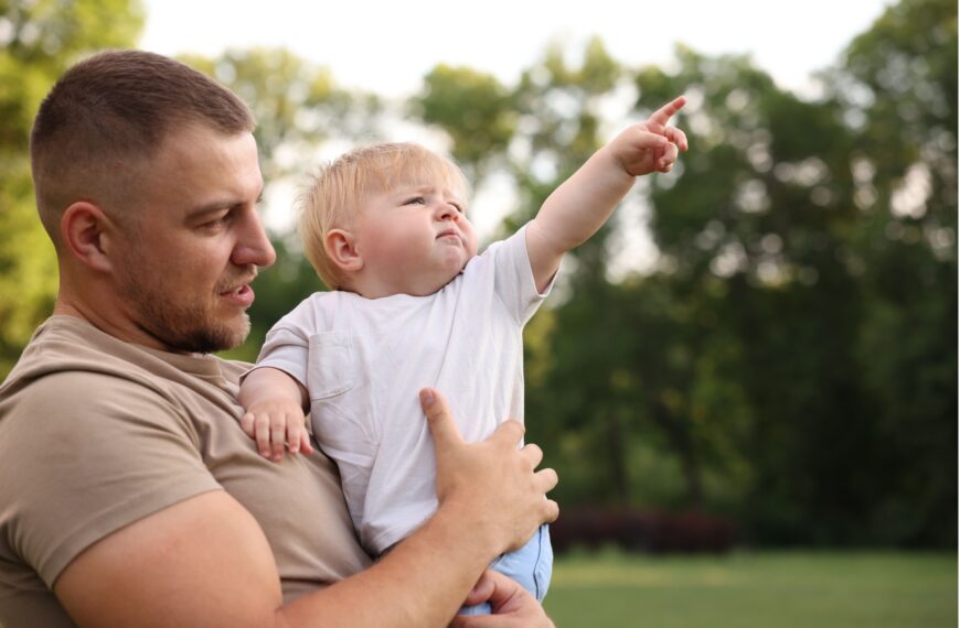 Father holding baby pointing outside.